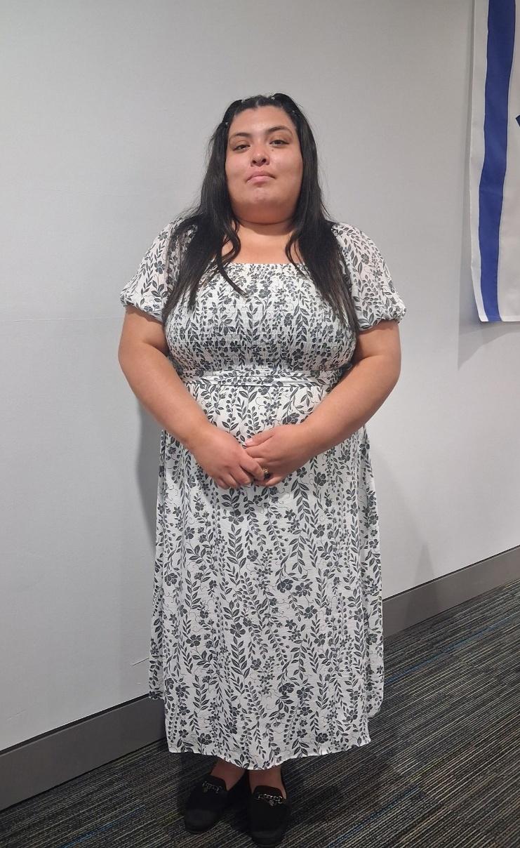 Graciela Castaneda standing in a white floral dress in front of a light wall